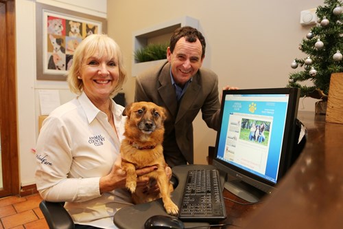 two people with a dog sitting next to a computer